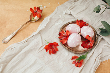 Modern Easter eggs with red flowers on linen cloth and spoon with petals on rustic wooden table. Stylish pastel pink Easter eggs painted in natural dye from beets. Happy Easter