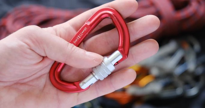 Red D-shape locking carabiner with strength ratings, used for climbing, held in a male hand - close up.