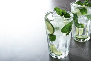 Tasty Mojito cocktail with ice cubes on light grey table, closeup. Space for text