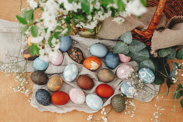 Fototapeta na wymiar Happy Easter. Easter eggs on rustic background with basket, spring flowers and green branches, rural flat lay. Stylish colorful Easter eggs with modern ornaments painted with natural dye