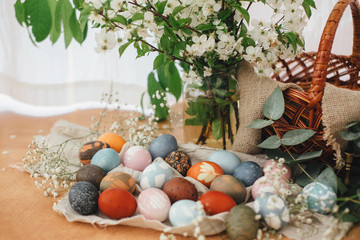 Obraz na płótnie Canvas Easter eggs on rustic background with basket, spring flowers and green branches, rural still life. Stylish colorful Easter eggs with modern ornaments painted with natural dye. Zero waste