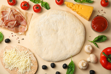 Flat lay composition with dough and fresh ingredients for pizza on beige background