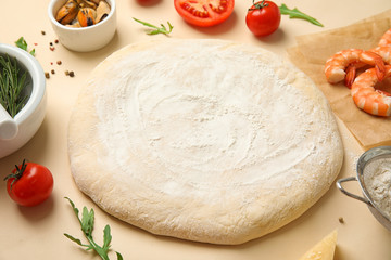 Dough and fresh ingredients for seafood pizza on beige background