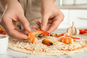 Obraz na płótnie Canvas Woman adding shrimp to seafood pizza at white marble table, closeup