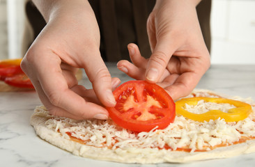 Woman adding tomato to pizza white marble table, closeup
