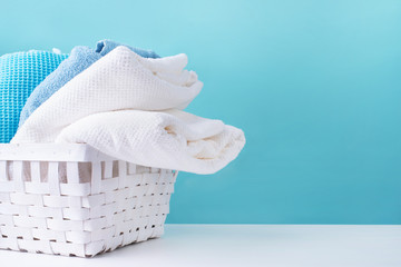 stack of clean towels in a white laundry basket on blue background - obrazy, fototapety, plakaty