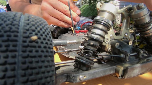 Man's hands screwing screw in a remote buggy car. Close up using screwdriver.