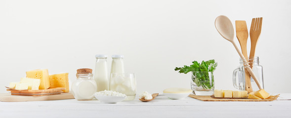 Different fresh dairy products on rustic background with milk, cheese, butter, eggs, greens,...