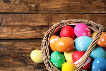 Colorful Easter eggs in basket on wooden background, top view. Space for text