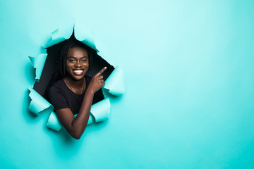 Young afro american woman pointed side posing from green paper hole