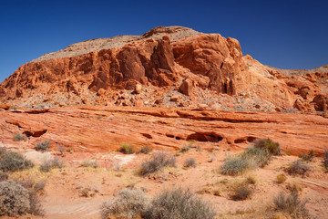 Obraz premium Mountains surrounding Fire wave during wonderful sunny day with blue sky, in Valley of Fire State Park, Nevada, USA