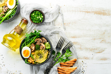 Buddha bowl: avocado, chickpeas, mushrooms, egg and arugula in a black bowl. Top view. Free space for text.