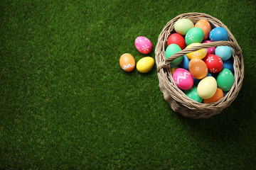 Colorful Easter eggs in basket on green grass, above view. Space for text