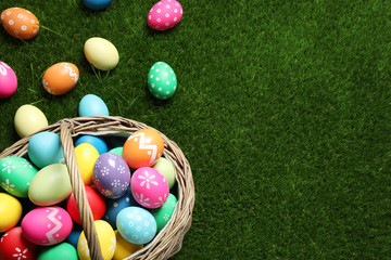 Colorful Easter eggs in basket on green grass, above view. Space for text