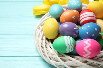 Fototapeta na wymiar Colorful Easter eggs in decorative nest on light blue wooden background, closeup