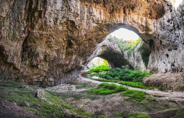 Devetashka cave interior, near Lovech town, Bulgaria. Panorama of entrance tunnel with hole on top and deep green grass