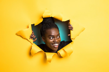 Young afro american woman posing from yellow paper hole
