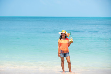 Happy Asian woman, a sexy Thai lady, drinking coconut water at turquoise sea  during  holidays  trip outdoors at natural ocean at island , Thailand.