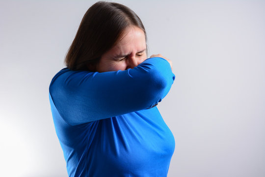 Unhappy Woman Cough Into Her Elbow, Not Her Hand. Woman Pull The Collar Of Her T-shirt Up To Cover  Mouth When Coughing. Coughing Advice From Experts Who Seek To Minimize Risk Of Viral Transmission 