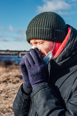 man in a hat, jacket and gloves blows his nose. face shield against viruses