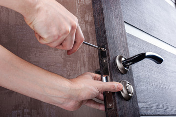 Handyman with a screwdriver installs and adjusts steel door lock in a wooden casement. Locksmith...