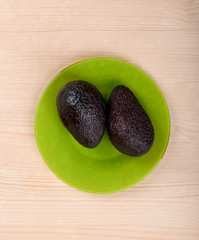 Ripe avocado fruits on a green plate over a wooden background.