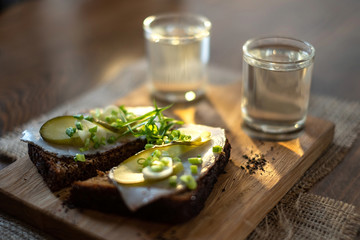 Sandwiches with two shots of vodka on wooden tray on table