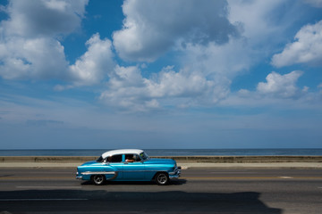 A classic blue car driving through the streets of Havana