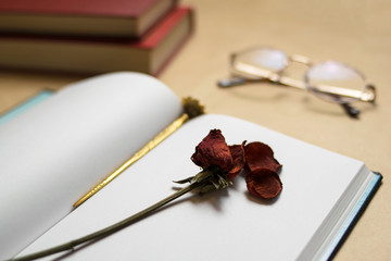 dry rose on notebook, with books and glasses
