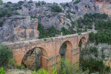 Fototapeta na wymiar Ancient roman aqueduct with a man walking on it surrounded by rocky mountains in Chelva, valencian community, Spain