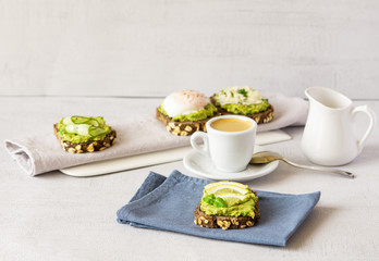 Variety of sandwiches, cup of coffee and milk for breakfast , snack, appetizer - avocado puree, poached egg, cucumber, lemon, whole grain bread. Grey background, banner. Vegetarian food. Ready to eat