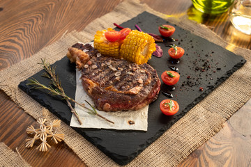 Steak with tomatos and corn on plate on wooden table