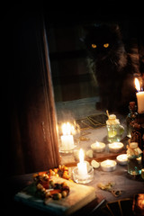 Reflection of a black cat, burning candles and fortune-telling cards in an old mirror