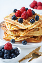  Homemade waffles with raspberries and blueberries in a plate on a white table