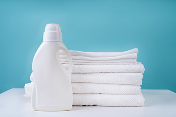 Fototapeta na wymiar stack of clean white towels and a bottle of detergent on blue background