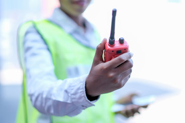 Hand of technician worker woman hold and shows red walky-talky in cargo container area with concept of good communication.