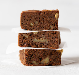 Stack of homemade chocolate brownie with nuts. Layer of paper bеtween it. Close up chocolate cake. Macro photo. Grey background. Concept: pastry, American traditional dessert, bakery. 