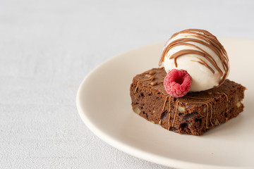 Piece of brownie with nuts, ice cream, strawberry, melted chocolate on a plate. Close up chocolate cake. Copy space. Grey background. Concept: pastry, American traditional dessert, bakery
