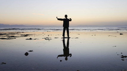 Silhouette of man practiceing qigong exercises at sunset by the sea.