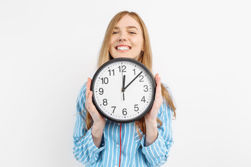 Happy girl dressed in her pajamas, holding the watch rejoices on a white background