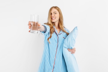 Young woman dressed in pajamas holding a glass of water on a white background