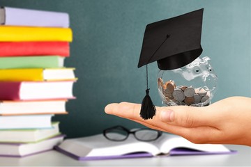 Graduation hat on a glass piggy bank with money in hand