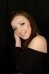 Naklejka premium beautiful brunette young girl happily smiling, hands in hair, looking at camera with fresh make up on black background, studio shot, vertical image