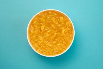 Diet nutrition healthy lifestyle. Yellow capsules with plant and fish oils supplements in white bowl on blue background