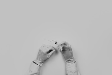 Medical doctor working place flat lay, faded monochrome. Top view of hands of MD holding syringe...