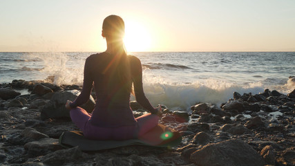 Rear view of female practice meditation at sea side at sunset.