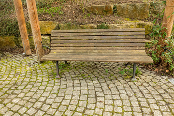 an empty wooden bench without people on a path with cobblestones in the park