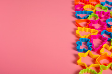 Multi-colored plastic molds of various shapes grouped on the right for making cookies on a pink background. Culinary concept. Flat lay with copyspace.