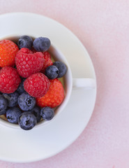 Fresh berries in a porcelain cup on pink concrete background