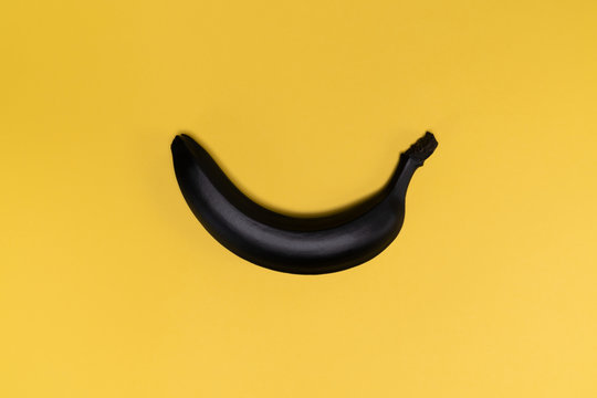 Matte black banana on the yellow background. The object is in the centre of the picture. Minimal style. Conceptual minimalism. Matte surface. Fruit. One